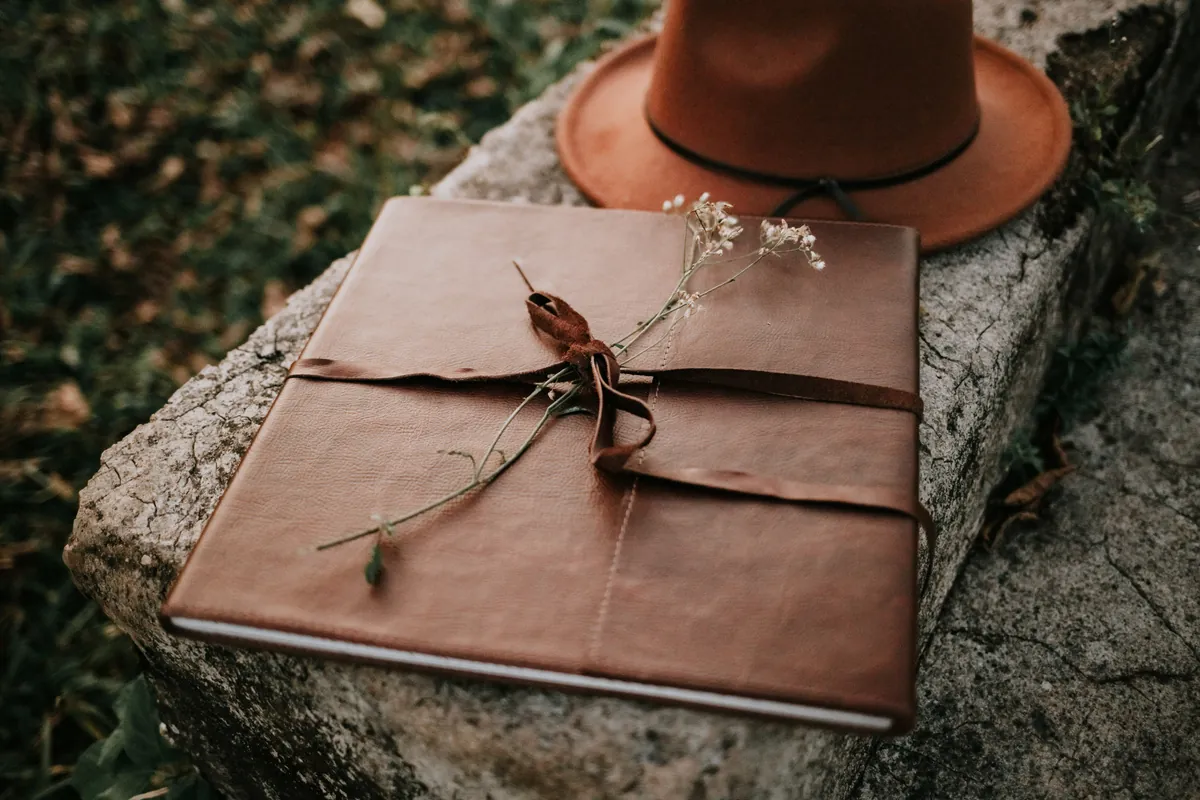 Álbum de couro com laço e flores secas ao lado de um chapéu